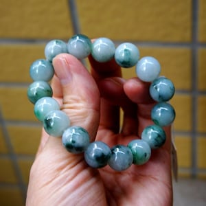 May include: A jade bracelet featuring green and white beads. The bracelet is crafted from natural jade and has a smooth, polished finish.