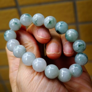 May include: A jade bracelet featuring light green and white beads. The bracelet is crafted from natural jade and has a smooth, polished finish.