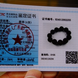 May include: A black beaded bracelet rests on a blue and white certificate. The certificate includes Chinese text, a red star, and a QR code. The bracelet is made of small, round, dark beads.