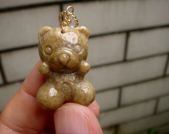 May include: A light brown jade bear pendant with a gold chain. The bear is carved in a cute, cartoon style with a bow tie.