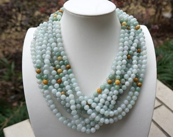 May include: A multi-strand necklace made of light green jade beads with a few yellow beads interspersed throughout. The necklace is displayed on a white mannequin bust.