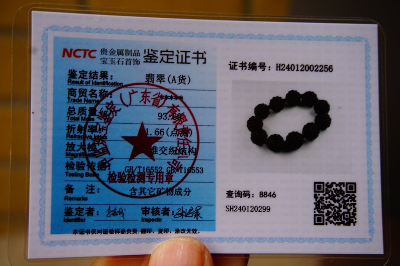 May include: A black beaded bracelet rests on a white document with Chinese text and a seal. The document also includes a QR code and the text "NCTC". The bracelet is made of round, dark beads.