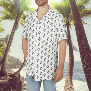 May include: A white short-sleeved button-down shirt with a palm tree print. The shirt has a relaxed fit and a collar.
