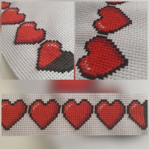 May include: Close-up of a white fabric with a row of red embroidered hearts. The hearts are stitched in a pixelated style, resembling a video game.