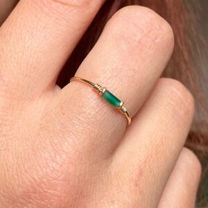 May include: A gold ring with a bright green rectangular gemstone. The gemstone is secured with gold wire. This elegant ring is a simple piece of jewellery, suitable for everyday wear.