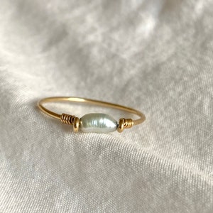 May include: A delicate gold ring with a single white pearl. The ring is simple and elegant, perfect for everyday wear.
