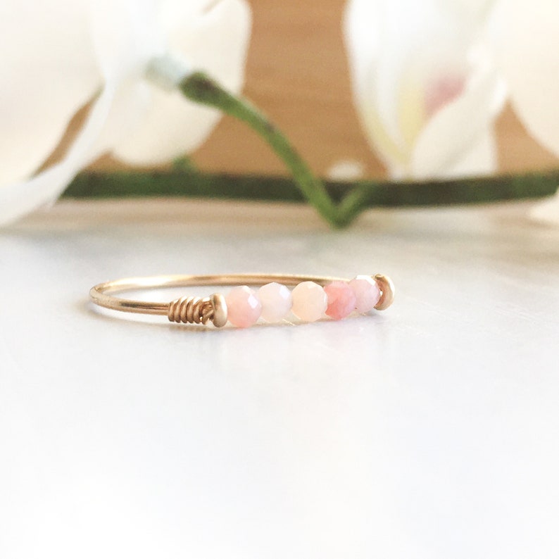 Pu&ograve; includere: Un delicato anello d'oro con una fila di perline rosa e bianche. La fascia dell'anello &egrave; sottile e avvolta con filo ad un'estremit&agrave;, con un design semplice ed elegante. Le perline presentano una sfumatura di tenui tonalit&agrave; rosa.