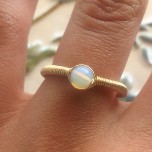 Puede incluir: Un anillo de alambre dorado con una piedra de &oacute;palo blanco.