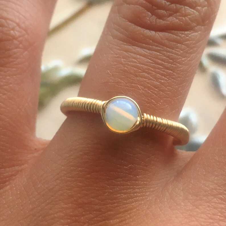Puede incluir: Un anillo de alambre dorado con una piedra de &oacute;palo blanco.