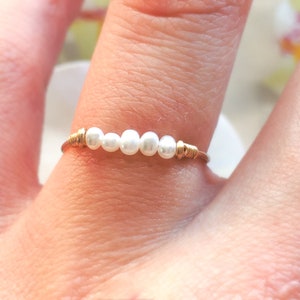 May include: A gold wire ring with five white pearls.