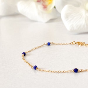 May include: A delicate gold chain bracelet with four small blue gemstone beads.