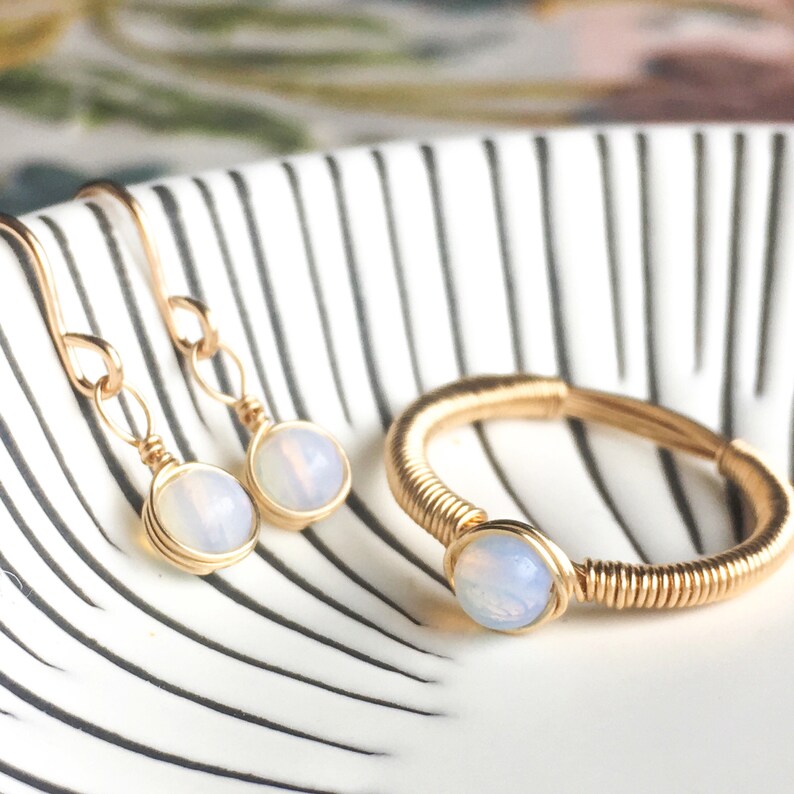 Puede incluir: Un conjunto de joyas de alambre dorado envuelto con piedras de &oacute;palo iridiscentes. El conjunto incluye un anillo y un par de aretes.