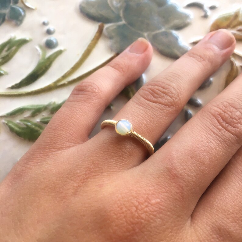 Puede incluir: Un anillo de alambre dorado con una piedra de &oacute;palo blanco.