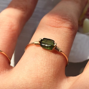 May include: A gold wire ring with a green tourmaline gemstone. The ring is on a person's finger.