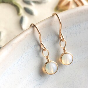 May include: A pair of gold earrings with small, round, white opal stones.