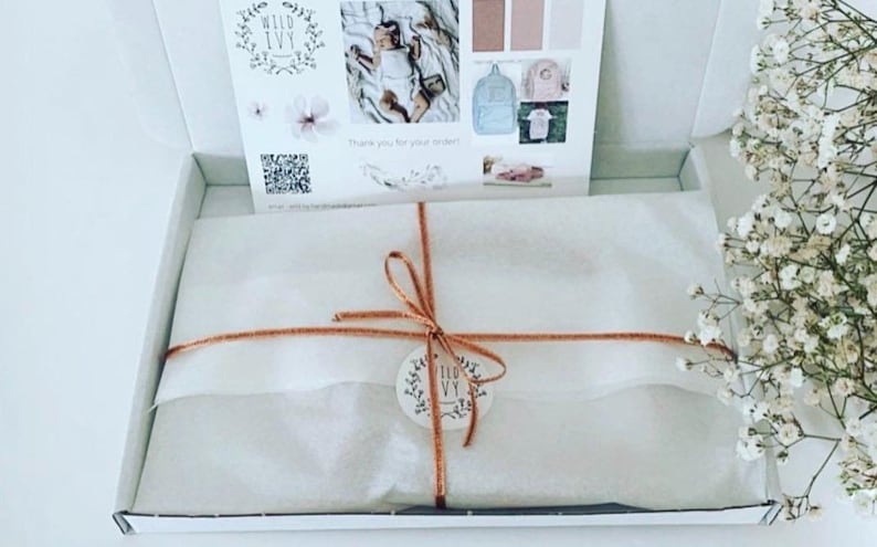 May include: A white cardboard shipping box containing a package wrapped in white tissue paper, tied with a copper-colored ribbon and a round Wild Ivy tag. A printed card with the Wild Ivy logo, a QR code, and product photos is inside the box.
