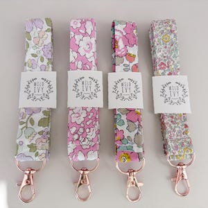 May include: Four floral fabric lanyards with rose gold swivel clasps. Each lanyard features a different pattern of flowers in shades of pink, purple, and yellow. The lanyards have a white tag that reads "WILD IVY".