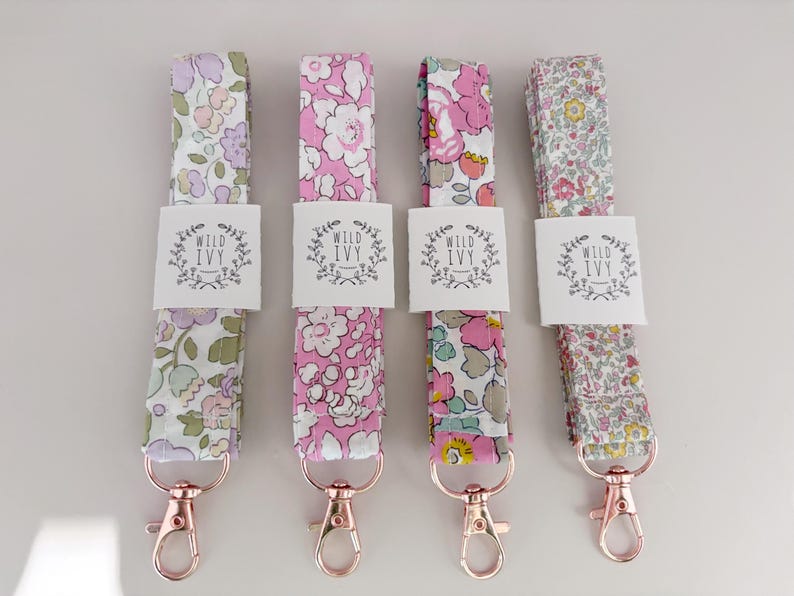 May include: Four floral fabric lanyards with rose gold swivel clasps. Each lanyard features a different floral pattern in shades of pink, purple, and green. White tags with the text "WILD IVY" are attached to each lanyard.