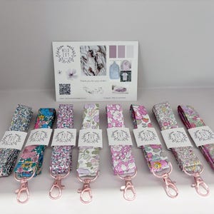 May include: A selection of floral lanyards with rose gold-coloured clasps. Each lanyard is wrapped with a white label with the text "Wild Ivy". A card with the Wild Ivy logo and other graphics is in the background.