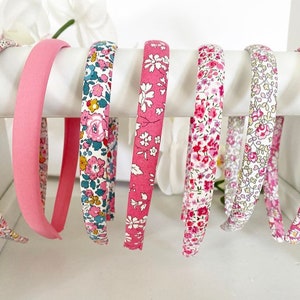 May include: A set of eight pink and white floral print headbands. The headbands are made of fabric and have a plastic base.