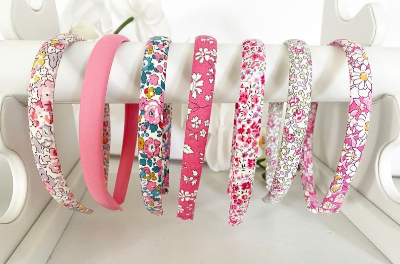 May include: A set of eight pink and white floral print headbands. The headbands are made of fabric and have a plastic base.