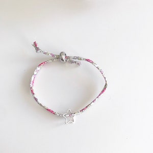 May include: A white and pink floral patterned fabric bracelet with a silver star charm and a silver bead.
