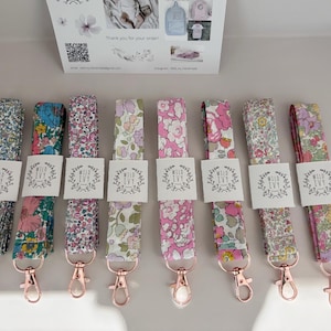 May include: A selection of floral lanyards with rose gold-coloured clasps. Each lanyard displays a different floral pattern in pinks, blues, and greens. The lanyards are labelled with a white tag that reads "Wild Ivy".