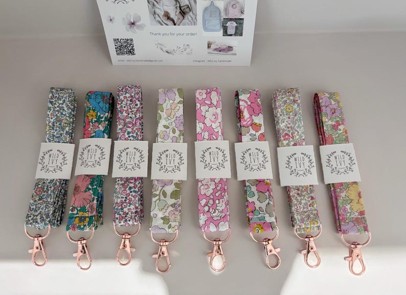 May include: A selection of floral lanyards with rose gold-coloured clasps. Each lanyard displays a different floral pattern in pinks, blues, and greens. The lanyards are labelled with a white tag that reads "Wild Ivy".