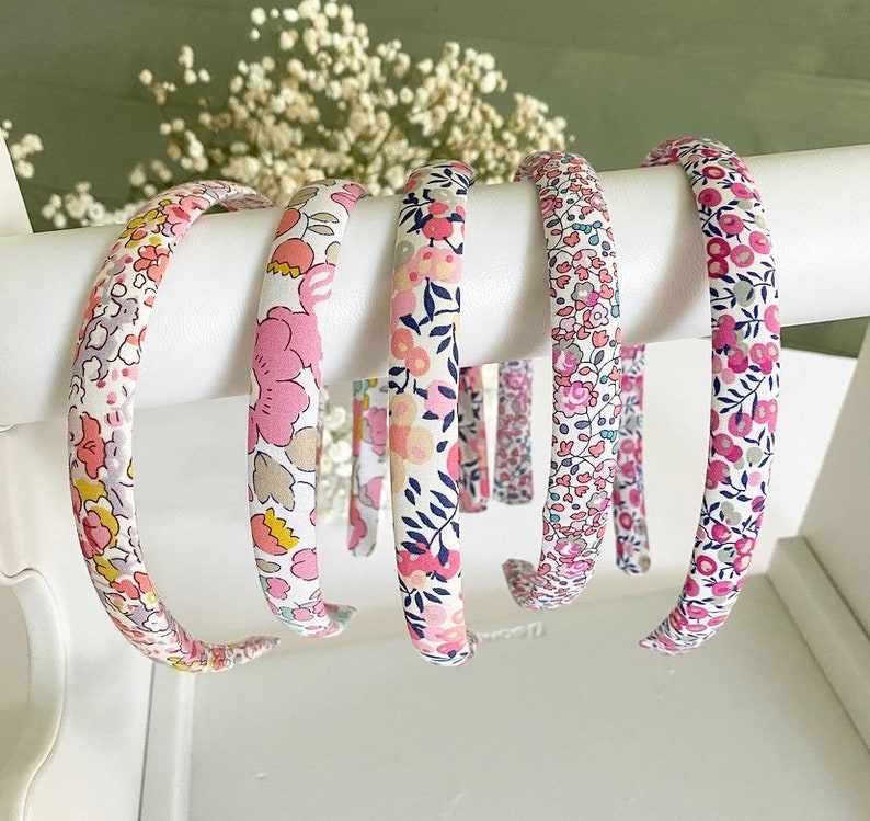 May include: Four floral patterned hair headbands in pink, white, and blue. The headbands are made of fabric and are a popular accessory for women.