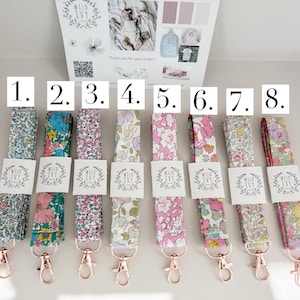 May include: Eight floral lanyards with rose gold clasps. Each lanyard displays a different colourful floral pattern, with a white tag that reads "Wild Ivy". The lanyards are arranged on a white surface.