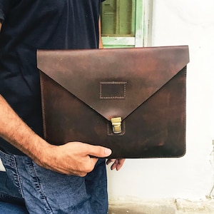 May include: A brown leather portfolio with a brass clasp. The portfolio has a flap that folds over and closes with the clasp.