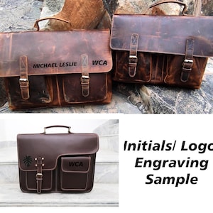 May include: Two brown leather briefcases with a flap closure and two front pockets. The briefcase on the left has the text "MICHAEL LESLIE WCA" engraved on the front. The briefcase on the right has a plant design engraved on the front. The text "Initials/Logo Engraving Sample" is displayed below the briefcases.