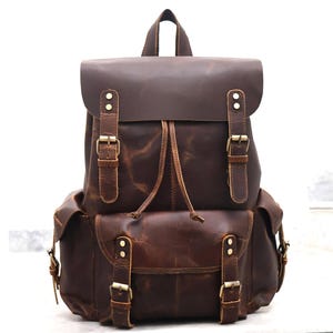 May include: A brown leather backpack with multiple pockets and buckles. The backpack has a drawstring closure and adjustable straps.