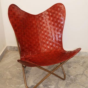 May include: A red leather butterfly chair with a woven design and a gold metal frame.
