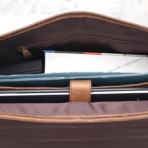 May include: A brown leather messenger bag with a zippered pocket and a flap closure. The bag is open and contains a laptop, a notebook, and other items.
