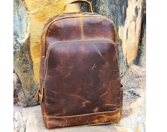 May include: A brown leather backpack with a zipper closure and a top handle. The backpack has a distressed look and is made of high-quality leather.