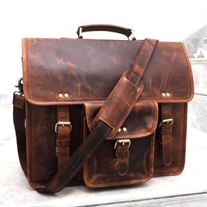 May include: A brown leather messenger bag with a large front pocket and adjustable shoulder strap. The bag has brass buckles and rivets.