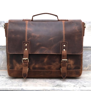 May include: A brown leather messenger bag with two adjustable straps and buckles. The bag has a flap closure and a top handle.
