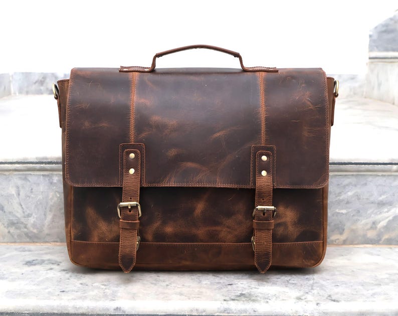 May include: A brown leather messenger bag with two adjustable straps and buckles. The bag has a flap closure and a top handle.