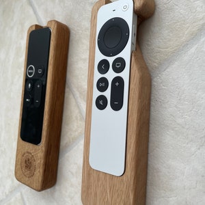 Oak case for Apple TV remote. smooth contoured corners, smooth finish. Remote sits flush into the holder and stays in position using micro suction pads. image shows both variants of the Apple TV remote on a desktop.