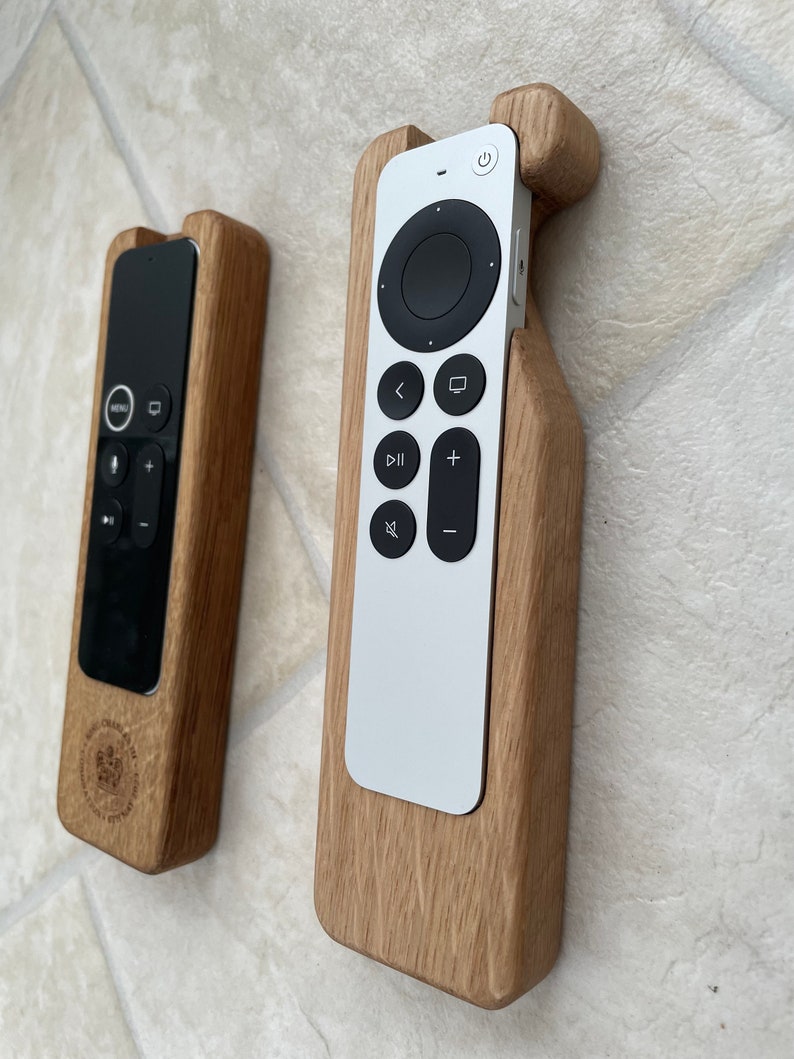 Oak case for Apple TV remote. smooth contoured corners, smooth finish. Remote sits flush into the holder and stays in position using micro suction pads. image shows both variants of the Apple TV remote on a desktop.