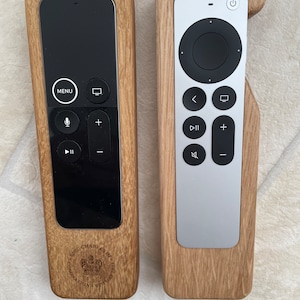 Oak case for Apple TV remote. smooth contoured corners, smooth finish. Remote sits flush into the holder and stays in position using micro suction pads. image shows both variants of the Apple TV remote on a desktop.