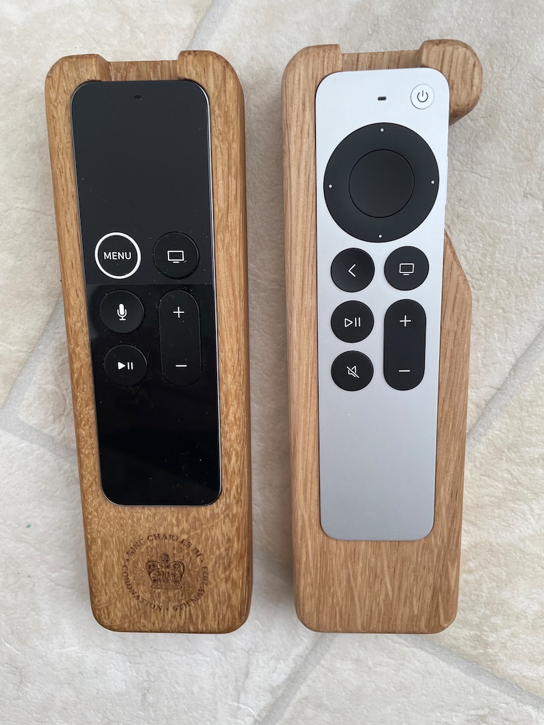Oak case for Apple TV remote. smooth contoured corners, smooth finish. Remote sits flush into the holder and stays in position using micro suction pads. image shows both variants of the Apple TV remote on a desktop.