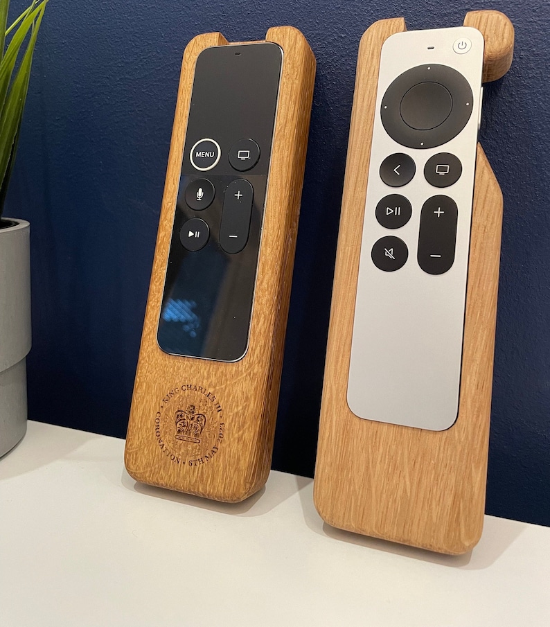 Oak case for Apple TV remote. smooth contoured corners, smooth finish. Remote sits flush into the holder and stays in position using micro suction pads. image shows both variants of the Apple TV remote on a desktop.