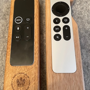Oak case for Apple TV remote. smooth contoured corners, smooth finish. Remote sits flush into the holder and stays in position using micro suction pads. image shows both variants of the Apple TV remote on a desktop.