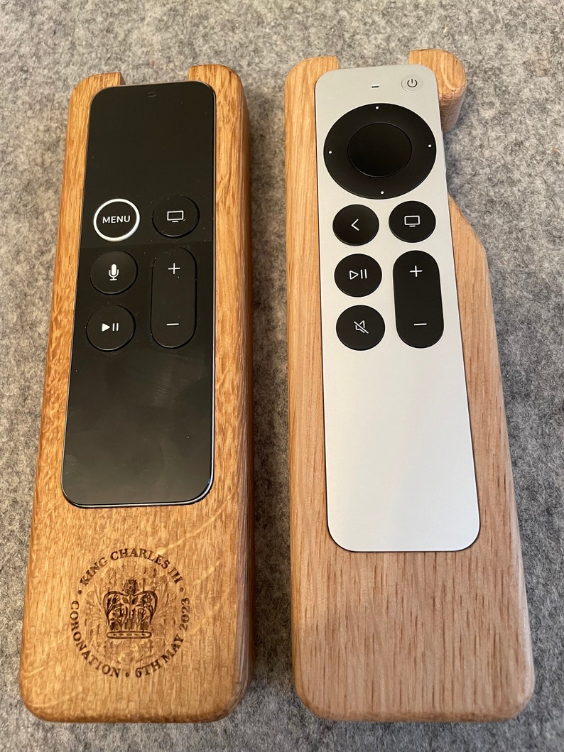 Oak case for Apple TV remote. smooth contoured corners, smooth finish. Remote sits flush into the holder and stays in position using micro suction pads. image shows both variants of the Apple TV remote on a desktop.