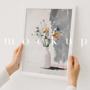 Pode incluir: Uma moldura branca com um passe-partout branco que envolve uma pintura de um buquê de flores brancas e amarelas em um vaso branco. O fundo da pintura é cinza claro com pinceladas.