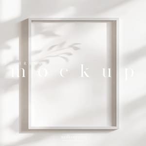 Może przedstawiać: Biały prostokątny makieta ramy z napisem "mockup" pośrodku. Rama jest ustawiona na białej ścianie z cieniami liści. Słowo "frame" znajduje się nad słowem "mockup".