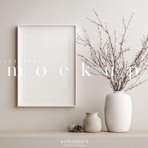 Op de afbeelding: Een witte, ingelijste blanco kunstafdruk mockup tegen een neutrale muur. Een witte vaas met takken en kleine witte bloemen staat naast een kleinere vaas en decoratieve items. De tekst "INTERIOR MOCKUP" wordt op de afbeelding weergegeven.
