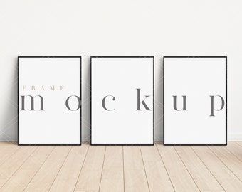 May include: Three black picture frames with white mats, arranged horizontally on a light wood floor. The frames are empty and ready for artwork. The text "FRAME MOCKUP" is printed in gray on the frames.